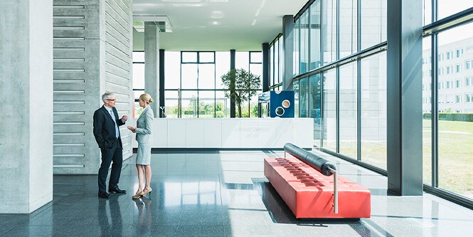 Lobby eines modernen Bürogebäudes mit zwei Geschäftsleuten, die sich unterhalten
