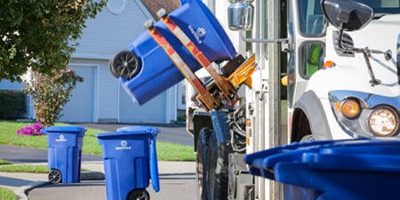 Eine blaue Recycling-Tonne wird auf einen Recycling-Lkw gehoben.
