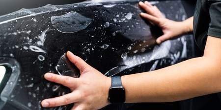 Person, die Lackschutzfolie auf einem Auto aufbringt
