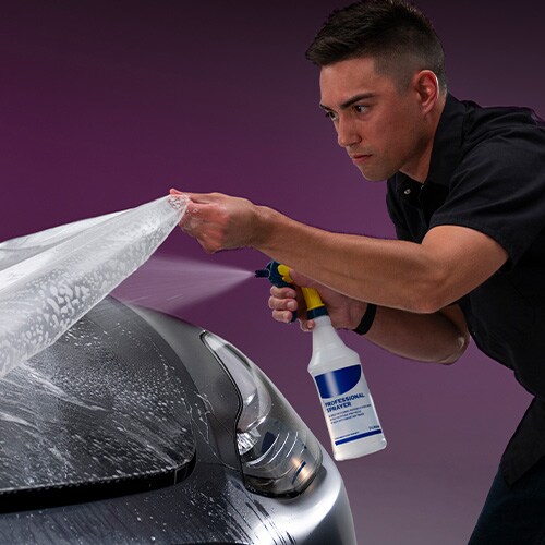 Mann sprüht Wasser auf die Motorhaube bei der Installation einer Lackschutzfolie