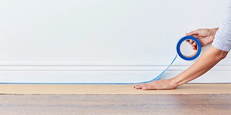 Person, die Kolophoniumpapier zum Schutz des Holzbodens mit 3M-Abdeckband befestigt
